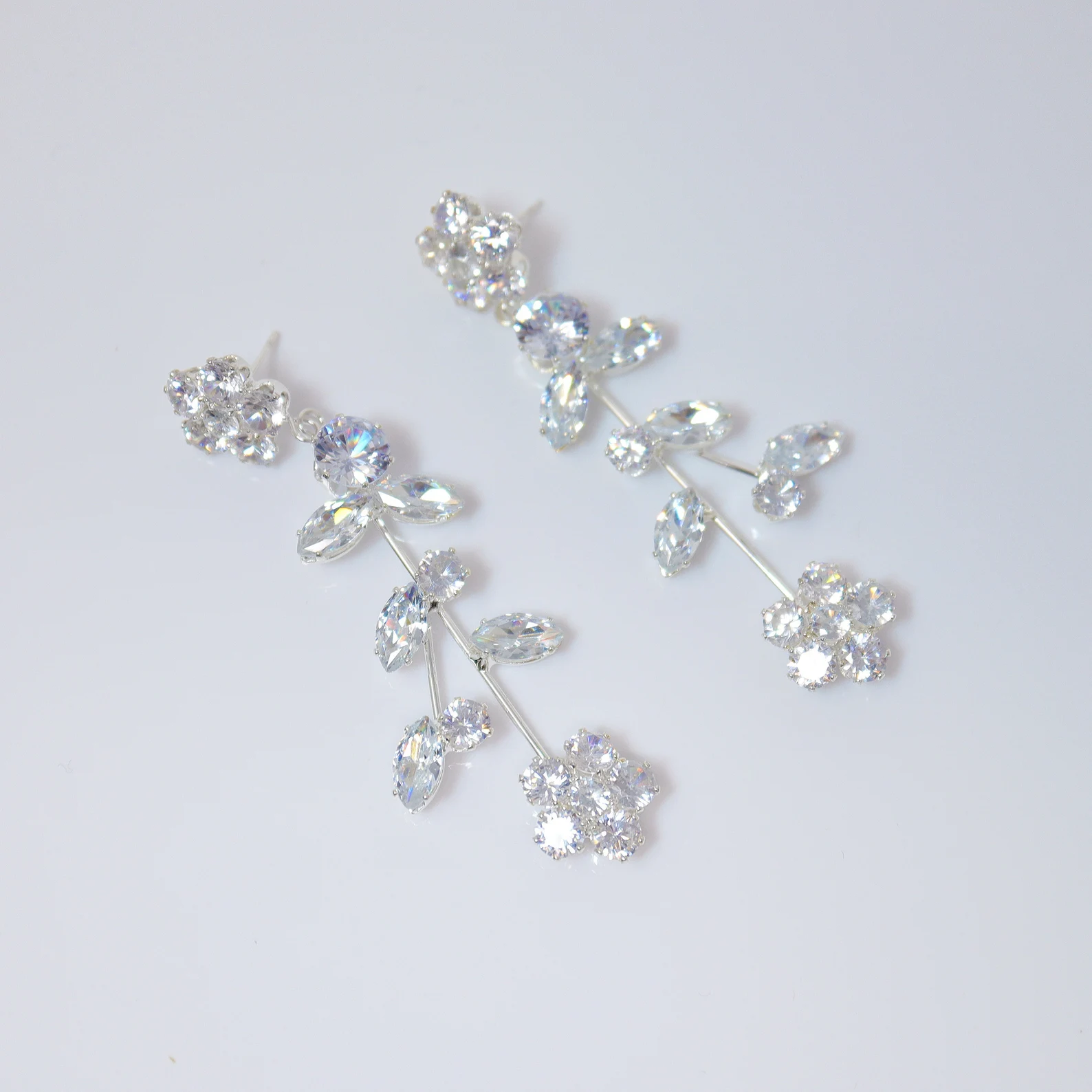 May include: A pair of silver dangle earrings with clear crystal stones arranged in a floral design.